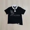 Camiseta de Verano de Manga Corta Estilo Ins Transfronterizo con Calavera de Pedrería Oscura, Diseño de Hebilla Metálica Lateral y Cuello Solapa, Top de Corte Holgado