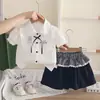 Nuevo atuendo de verano 2026 para niñas: conjunto elegante de manga corta con cuello, que presenta una camisa de dibujos animados y una falda corta, disponible para venta al por mayor