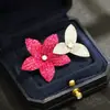 Elegante y sofisticado accesorio de broche floral con diseño intrincado, incrustación sin bordes de piedras de imitación rubí, y flores dobles unidas entre sí.