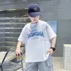 Verão 2026 Novo Estilo Camiseta Infantil Tendência Americana Cool Estampa de Letras Manga Curta Masculina Casual Gola Redonda Confortável para Crianças de Tamanho Médio e Grande