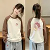 Camiseta infantil moderna e estilosa com blocos de cor, gola redonda, mangas compridas e estampa de desenho animado, perfeita como camada base para o outono e inverno de 2026