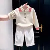 Ropa infantil coreana 2026 otoño e invierno nuevo estilo suéter de punto con cuello polo a rayas blanco roto pantalones blancos de pierna ancha modernos