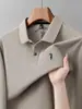 Camisa polo masculina de primavera e outono com design simples de mangas compridas, apresentando logotipos bordados e cor lisa e sólida, adequada para uso business casual.