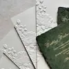 Elegantes y estilosas invitaciones de boda con relieve floral 3D y iniciales en pan de oro, hechas a medida por la fábrica