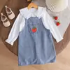 Conjunto de dos piezas fresco y lindo: camisa blanca de manga larga con cuello de muñeca para niña combinado con una falda tipo overol de mezclilla con bordado de fresas.