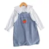 Conjunto de dos piezas fresco y lindo para niña: camisa blanca de manga larga con cuello de muñeca combinado con una falda de mezclilla con tirantes bordada de fresas.